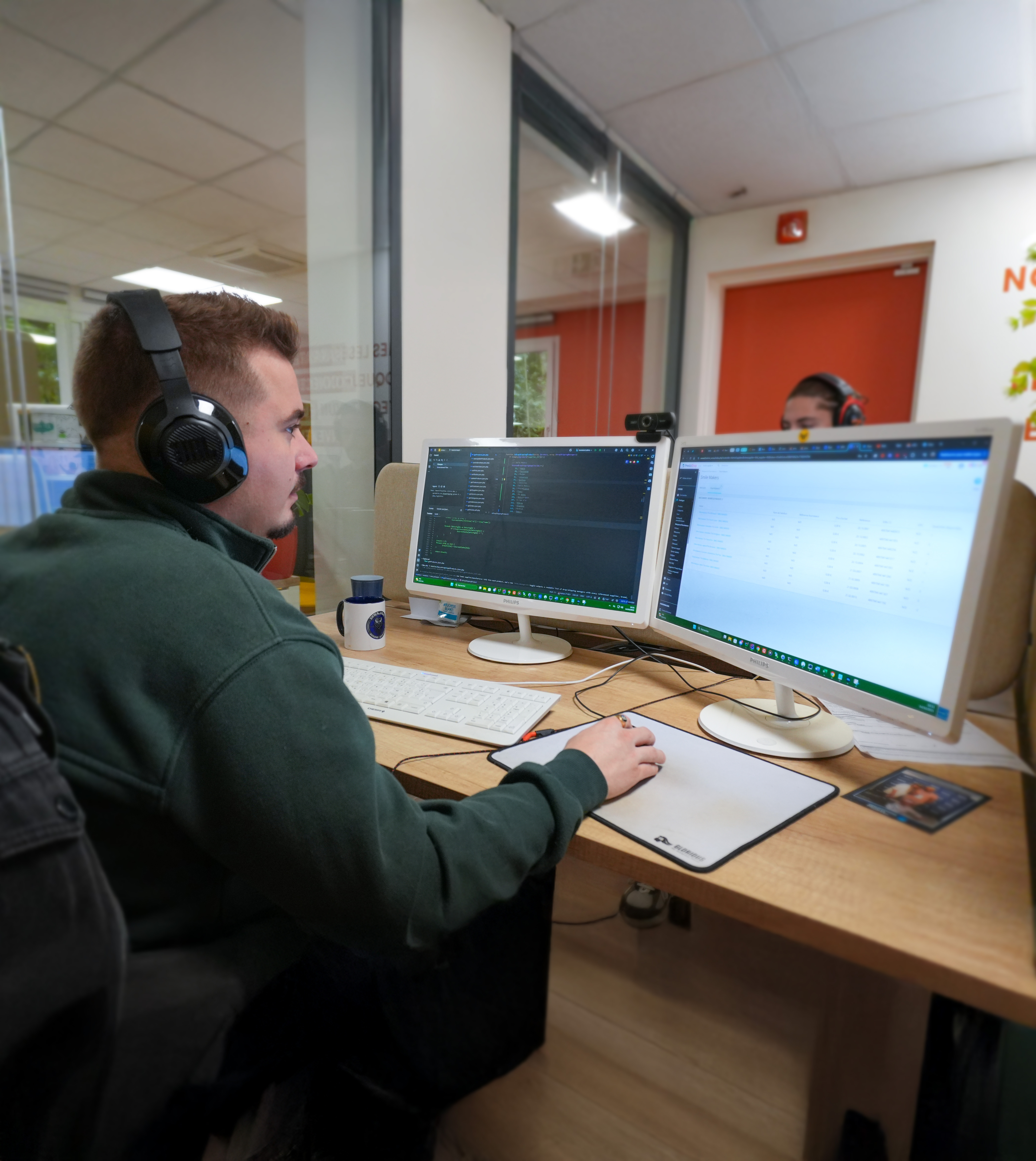 Un homme travaillant sur deux écrans d'ordinateur avec un casque audio dans un bureau moderne, en train de coder ou de gérer des logiciels.