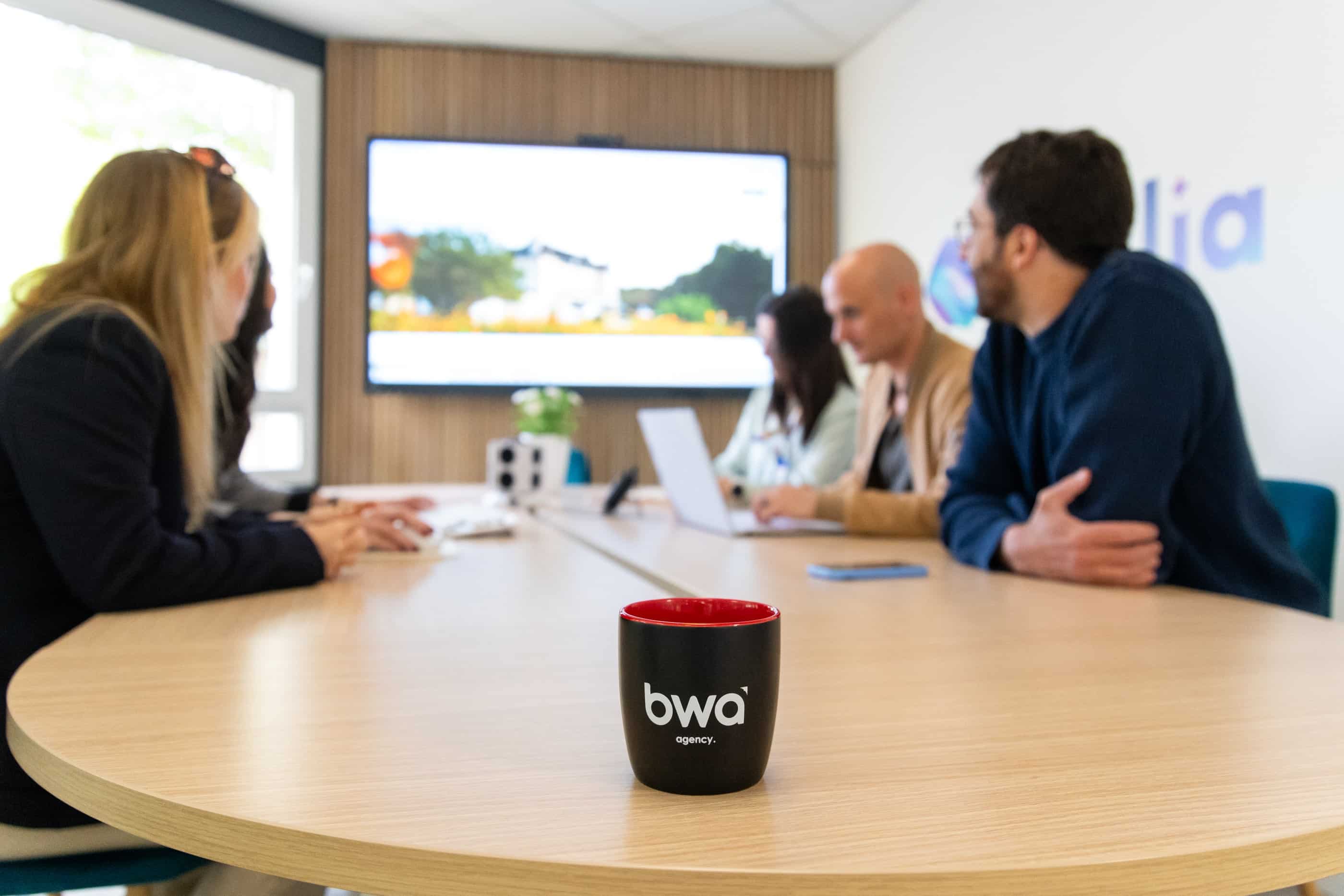 Réunion d'équipe dans une agence web avec un mug personnalisé sur la table, participants discutant autour d'une table de conférence.
